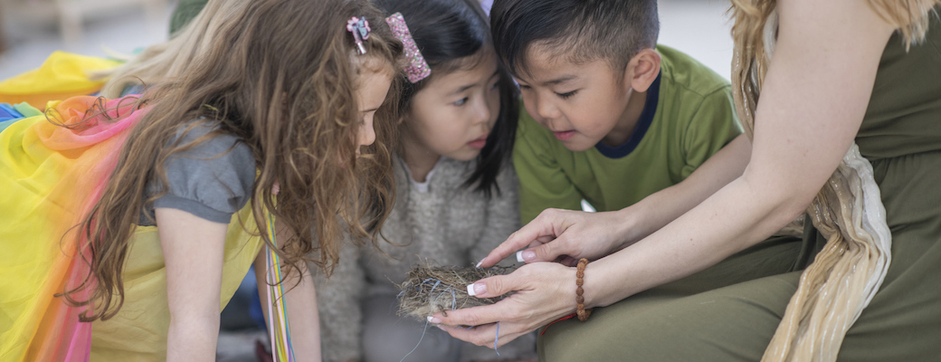 A teacher holding a small nest while three children lean in to look closely